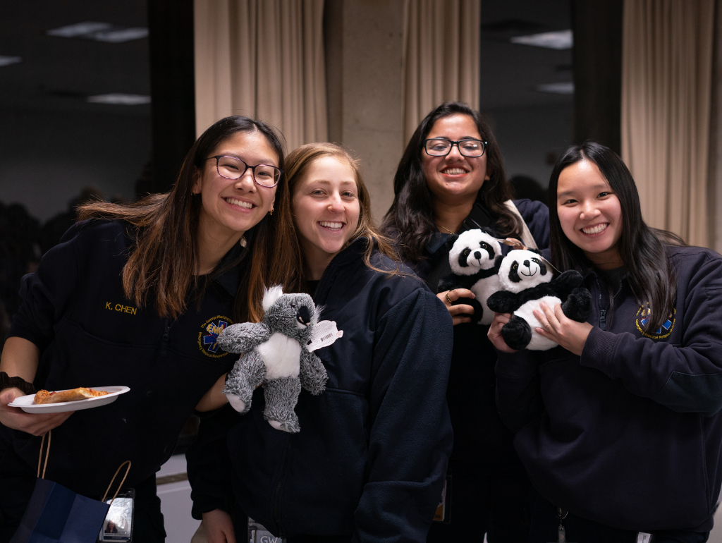 Four students pose for a photo holding plates of food and their plush study buddies