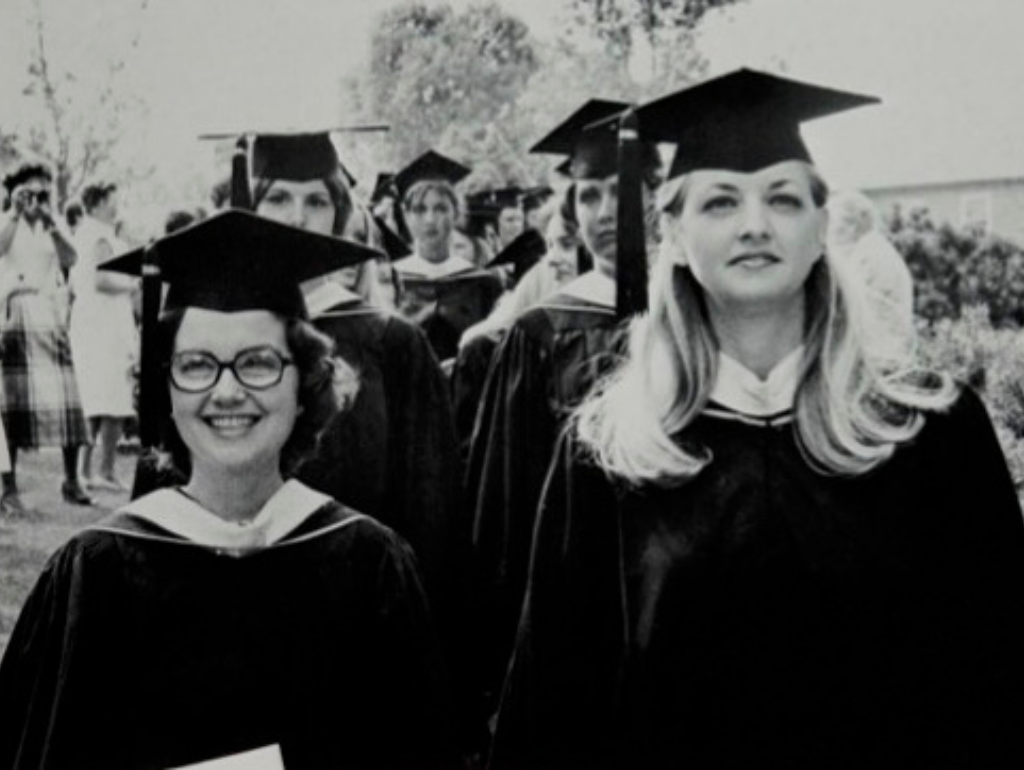 Black and white image of two lines of graduating women in the graduation regalia caps and gowns