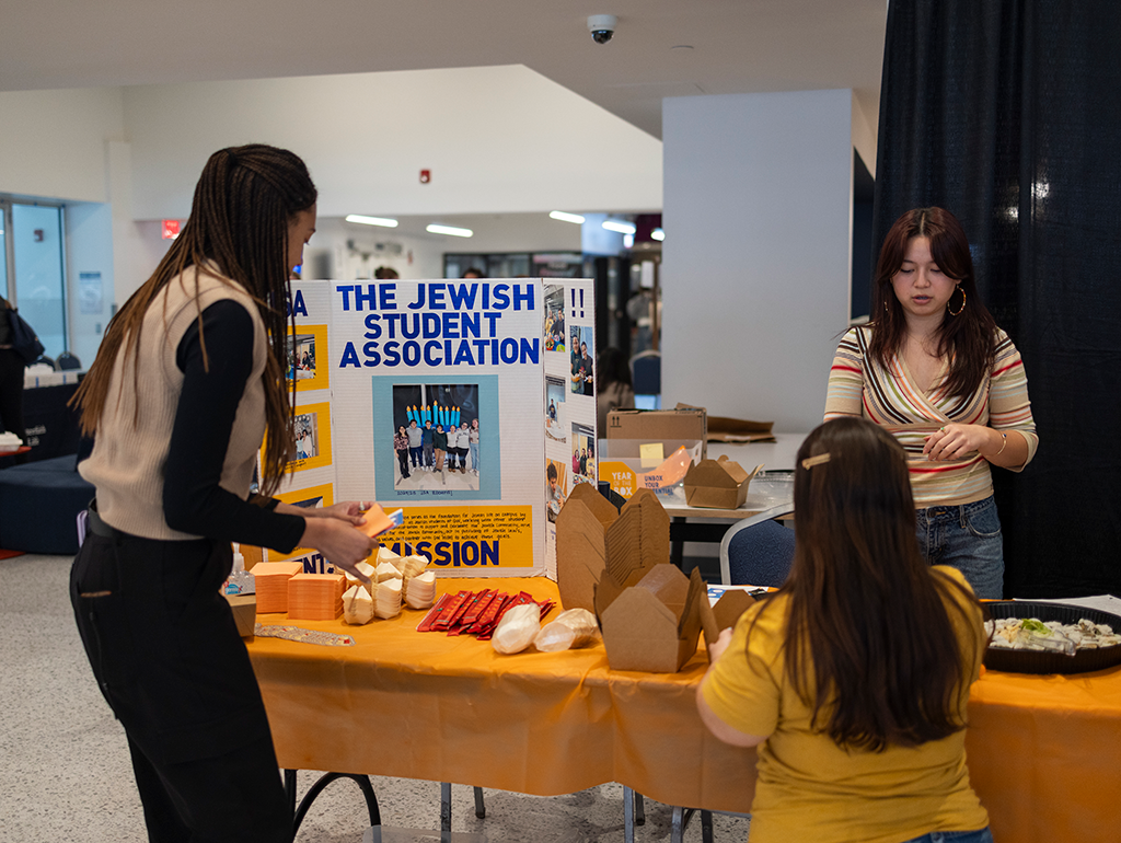 Three members of the Jewish Student Association Stand around table at the Kosher Food Festival