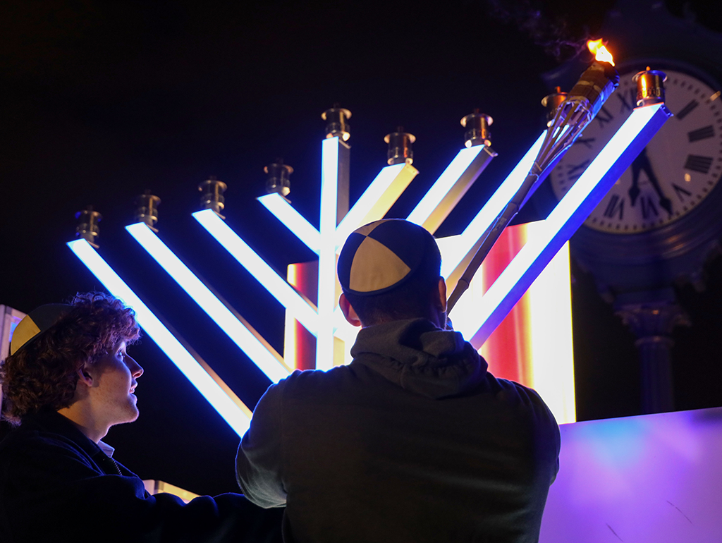Two students wearing yamakas standing in front of large light up menorah