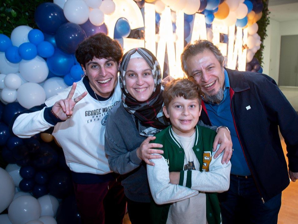 Family of 4 posing for a photo at Families Weekend with "GW AFW" lighted backdrop and balloons