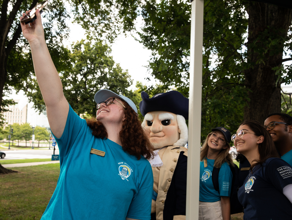 Three Orientation Leaders taking a selfie with the George Mascot