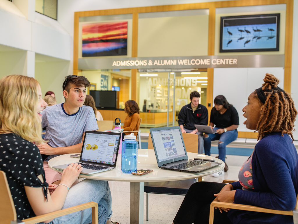 Three students talking together at a table with their laptops open in the University Student Center