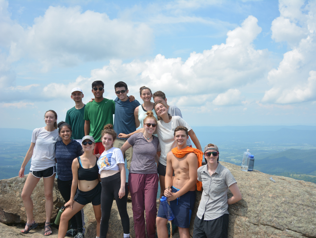 A group of students posing for a photo at the top of a mountain with a view of a valley behind them