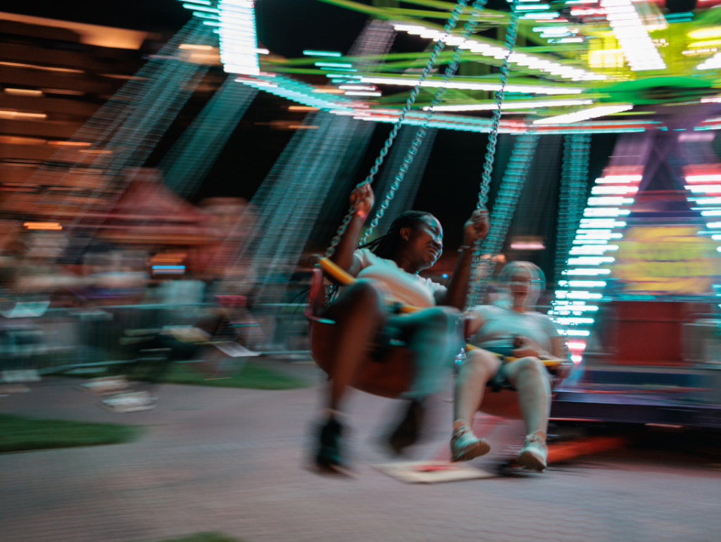 Students smiling and laughing on a light-up carnival swing ride in University Yard