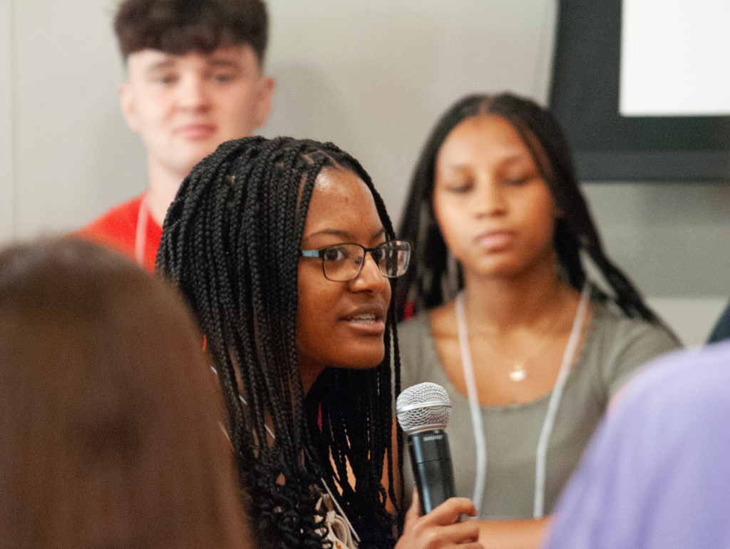 Student talking into a microphone surrounded by several peers