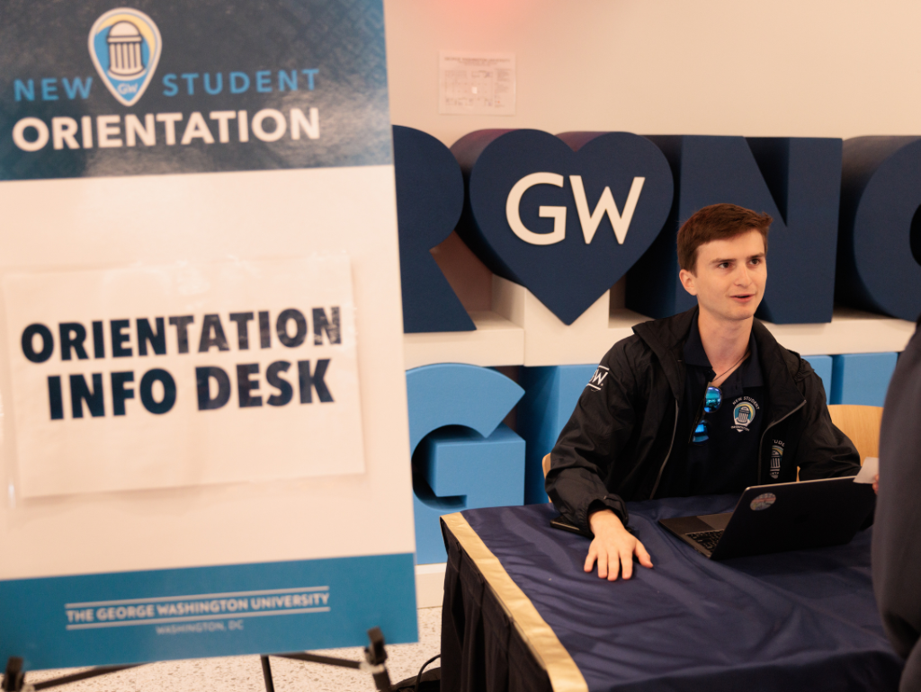 Student worker sitting behind a table with a sign that reads "Orientation Info Desk"
