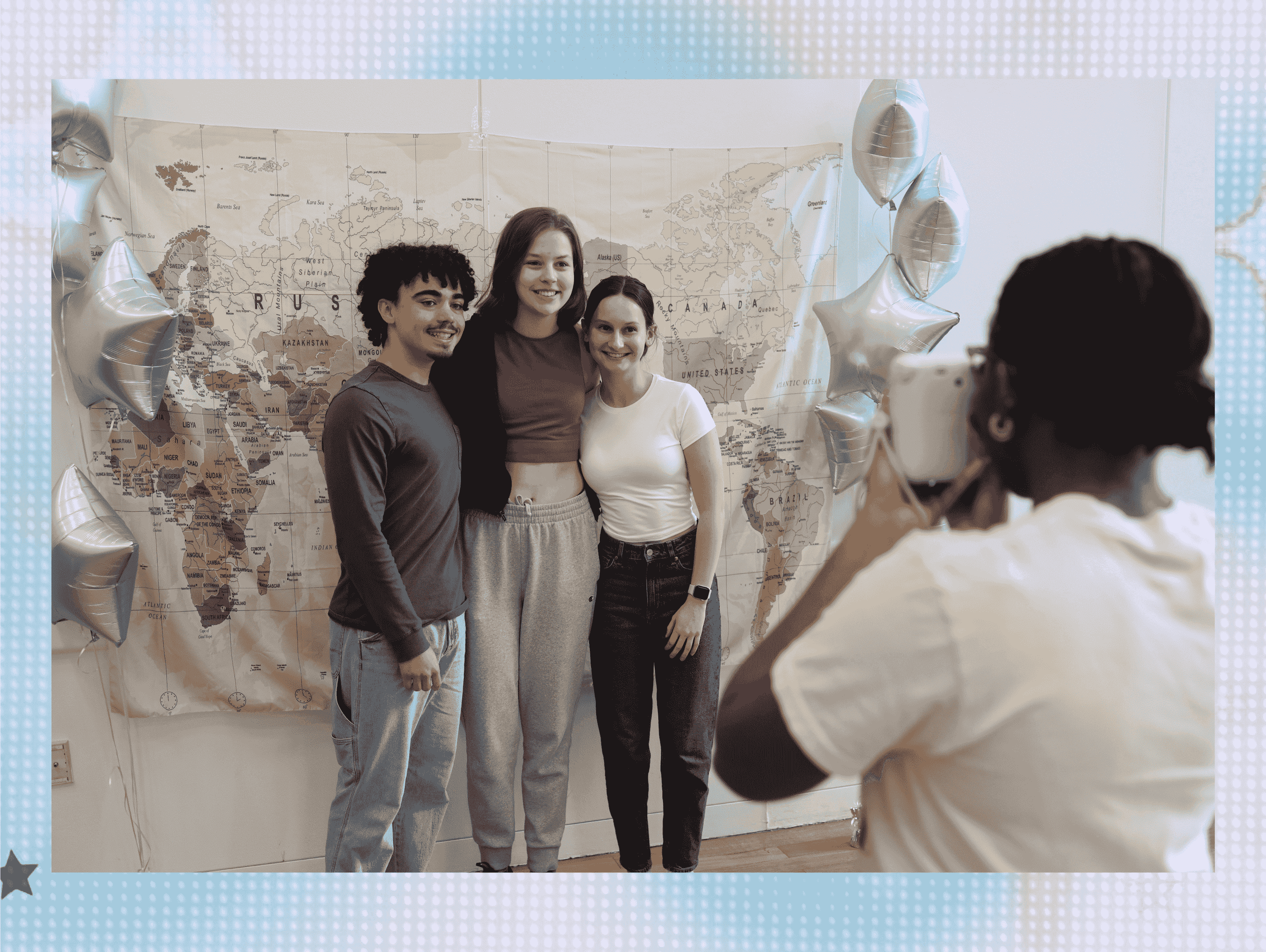 Three students stand in front of a backdrop, photographer is in front of them getting their picture taken