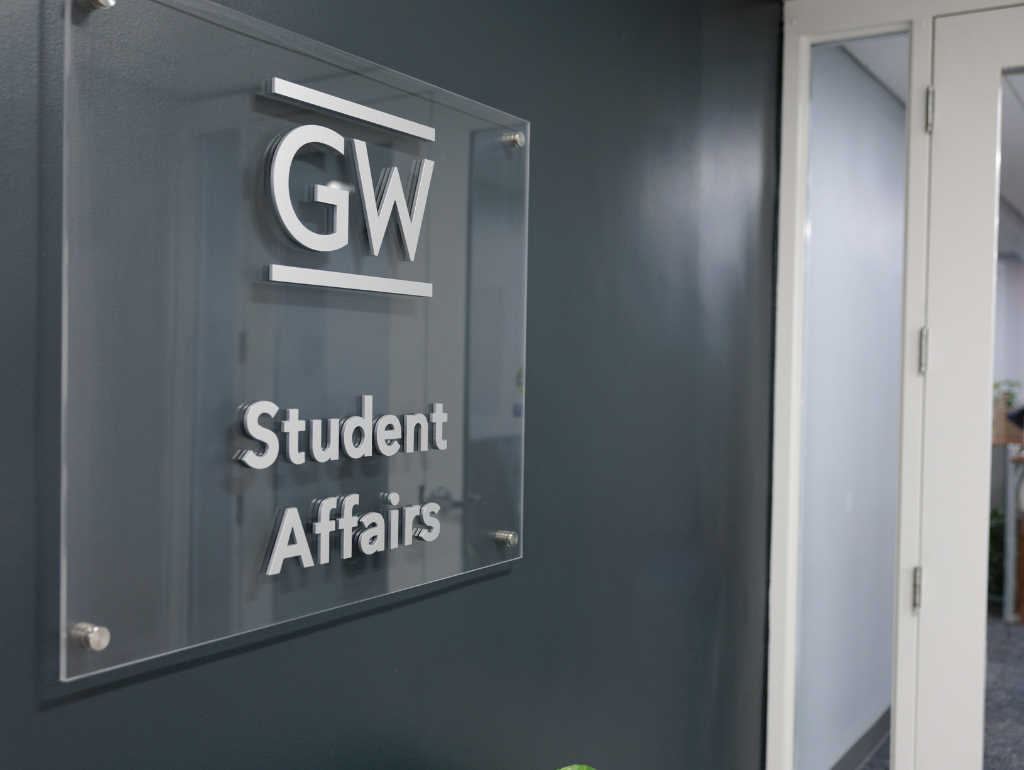 GW Student Affairs logo on an acrylic sign posted on a dark blue wall