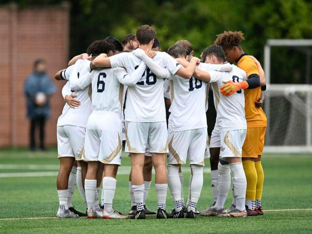 GW Mens Soccer team in a huddle on the field