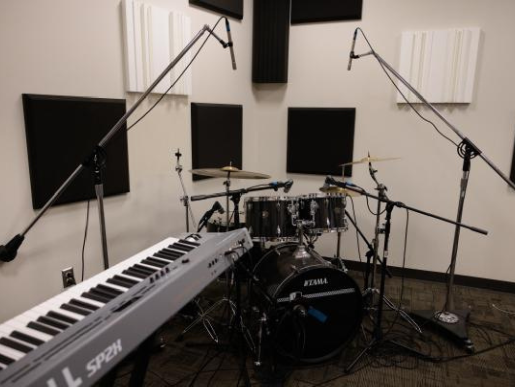 Electric piano, drums and microphones set up in a room with sound dampening walls