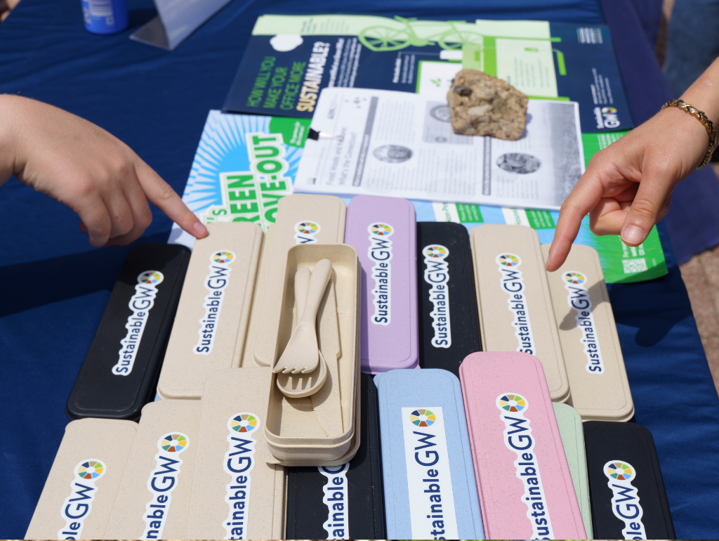 Sustainable GW table with two students pointing at a pile of reusable eating utensils and other resources