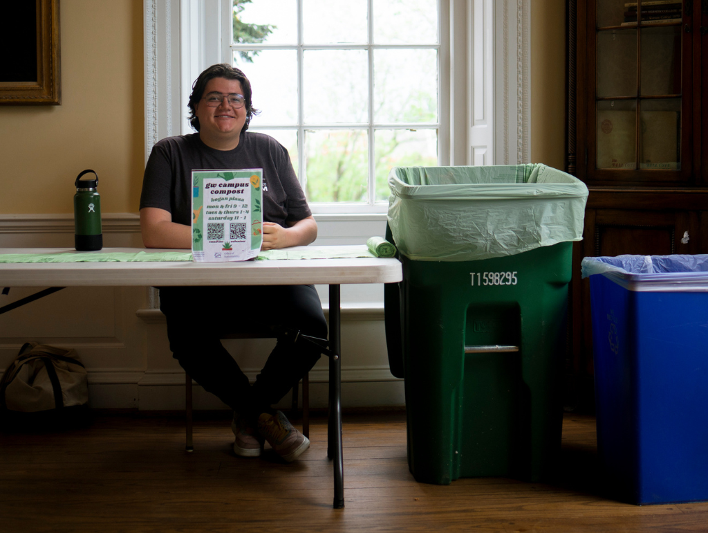 A student sitting at a composting table in Post Hall, smiling