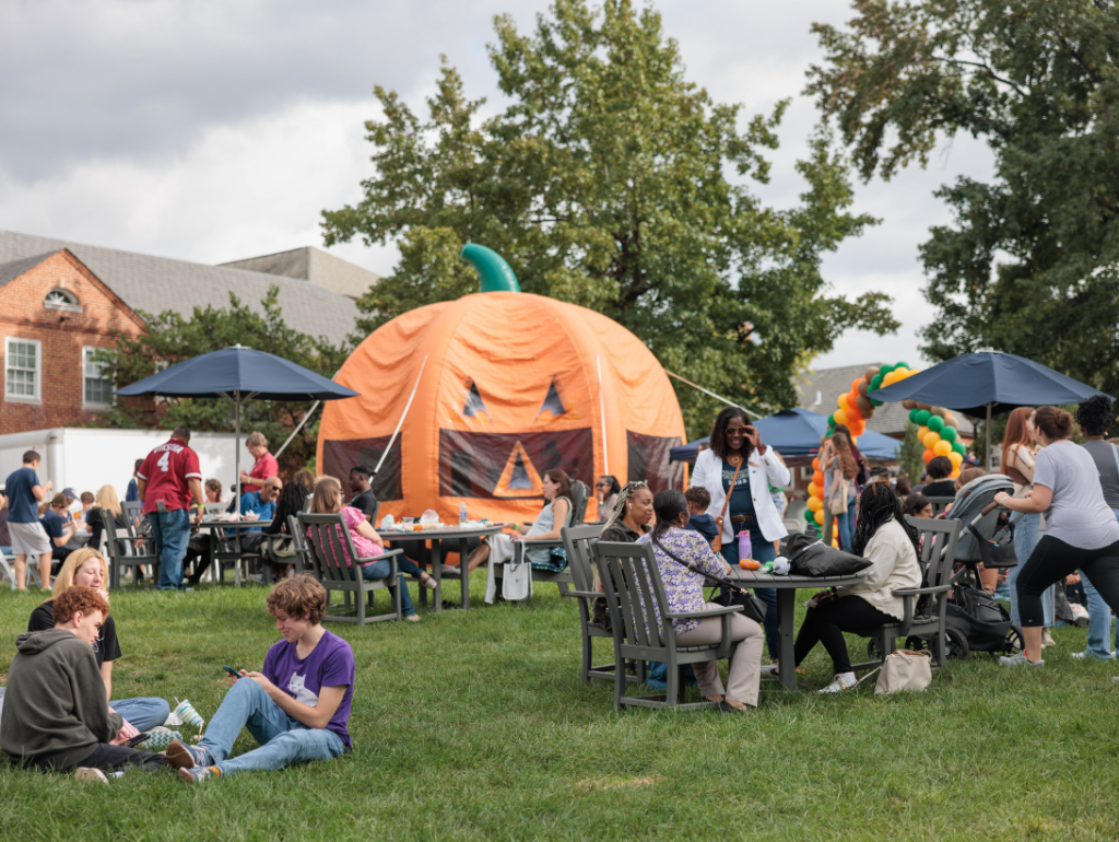 The MVC Quad filled with students and families at Vern Harvest, with fall decor, and a giant inflatable pumpkin in the background