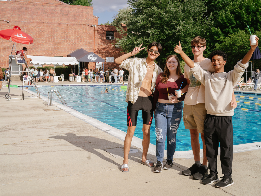 A group of four students posing and smiling beside the outdoor pool on the Vern on a sunny day