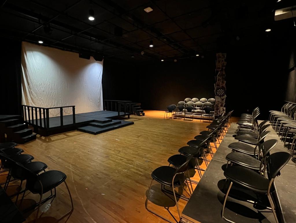Rows of chairs facing a small stage on a light wood floor